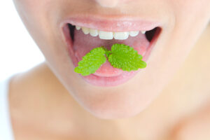 Close-up of a mouth with fresh mint leaves on the tongue.
