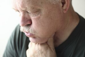 An elderly man coughing and holding his throat in discomfort.